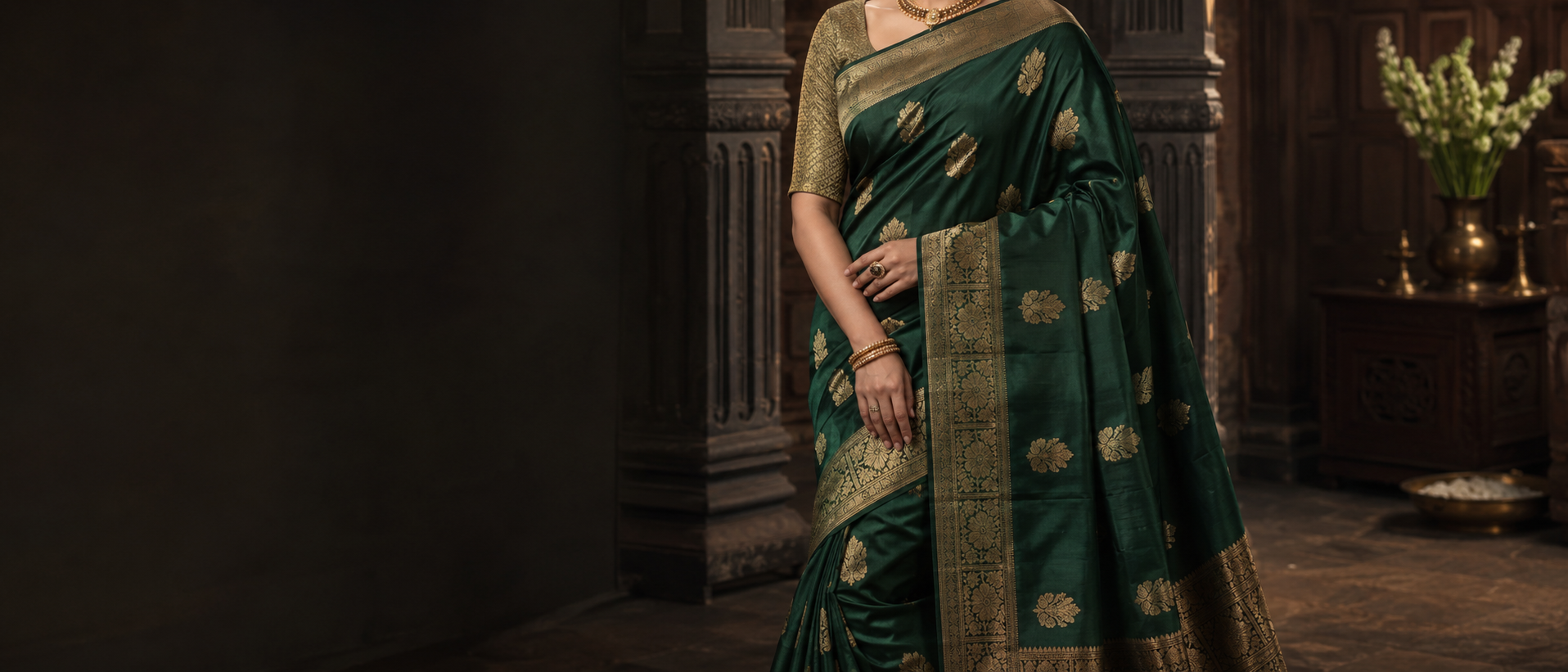 Model in an emerald green silk saree with a gold zari border, standing in a dimly lit carved archway